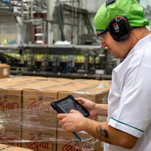 A person with ear protection using a tablet in a warehouse setting.