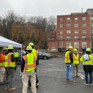 Employees standing outdise in a parking lot wearing high vis vests and hard hats.
