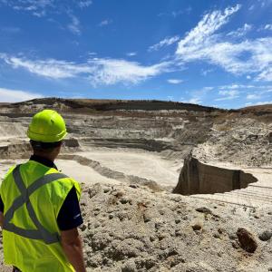 A person in a hard hat and high-vis vest looking out over a quarry area.
