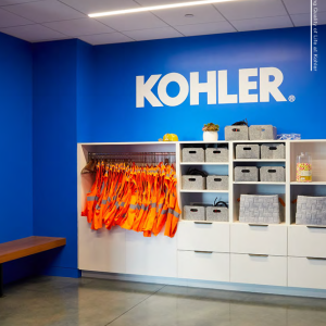 Kohler in white on a blue wall. Cabinets with drawers and a rack of orange safety vests.