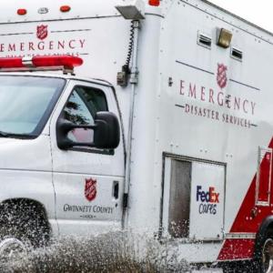 A box truck going through a puddle. Salvation Army and FedEx logos on the sides.