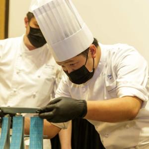 student in a chef's uniform carefully balancing a plate