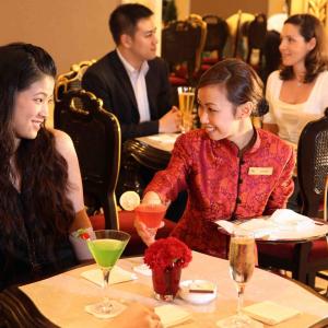 student in a red jacket places colorful cocktails on a small table