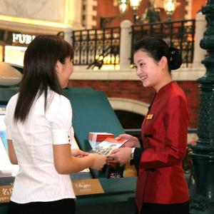 employee in a red jacket hands a brochure to a guest in a white shirt