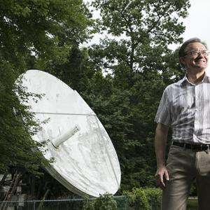A person standing outside looking to the sky, a large satellite dish behind them