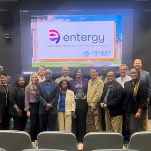 A group of people posed at the front of an auditorium. A digital display behind them with the entergy logo showing.