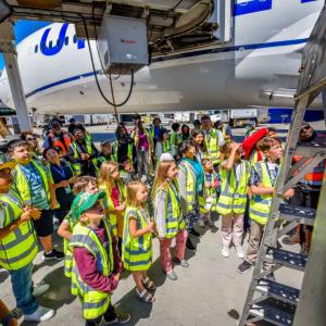 A group of kids and adults in high-vis vests looking up close at an airplane.