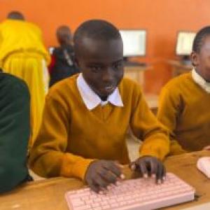 A smiling child using a computer next to others.