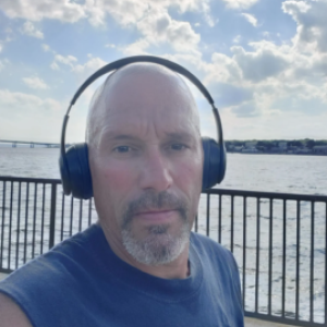 scott cabral wearing headphones, a railing and waterway behind him