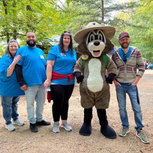 Four people and a mascot pose smiling for the camera outdoors.