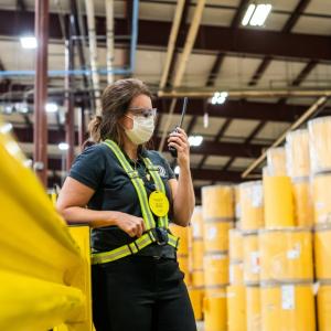 Karen Crisp in safety gear standing among yellow barrels in a factory