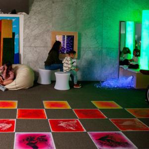 Inside the sensory room. Color changing floor tiles, a bubble tower in the corner and families playing.