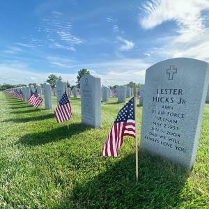 Close up of a headstone at a service member cemetery. American flags planted in front of each stone.
