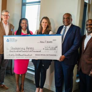 Five people posed with a large check made to Sheltering Arms.