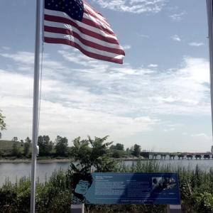 two flags on poles, a water way and peninsula behind them