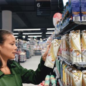 A person in a grocery store, selecting a box from a shelf.