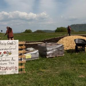 Volunteers working outside with a sign on wooden pallets that reads "Help GWES' Garden Grow Volunteers Are Welcome This FRIDAY at 4:00"