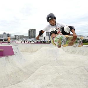 a skateboarder doing a trick in a cement skate park, tall buildings in the background