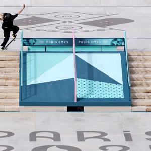 A person skateboarding over stairs "Paris 2024" on the cement at the bottom of the staircase.