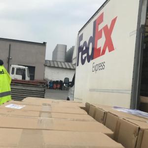 view from the top of a row of boxes towards a person checking them. A fedex truck to the right