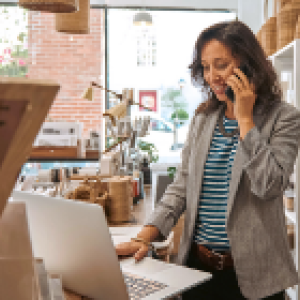 A person in a shop using a phone and working on a laptop