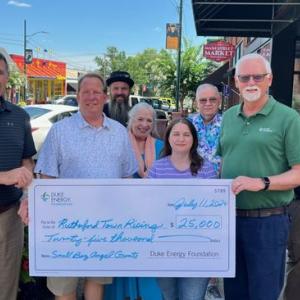 A group of people posed with a large check on a sidewalk.