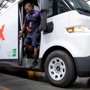 Smiling employee exiting a FedEx electric vehicle