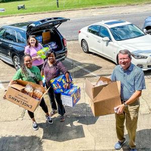 a group of four people unloading snacks and food from the back of a car