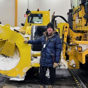 A person standing next to a large snow plow.
