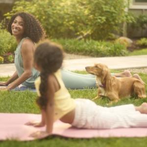 Adult and child doing yoga on a lawn with a dog nearby