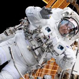 An astronaut in a space suit in outerspace, a space station behind them.