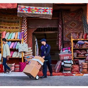 A person delivering boxes at a shop with colorful textiles hanging.