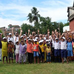 A group of youth and adults posed outside with arms up.