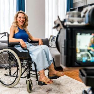 Photo of a woman in a wheelchair in front of a camera. 