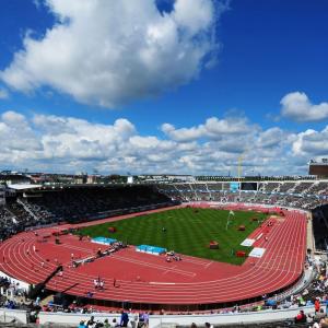 aerial view of a large stadium filled with spectators, a blue sky with few clouds