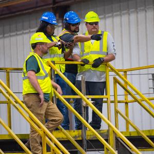 Four employees in hard hats and high-vis vests standing on a platform. One pointing to the distance.