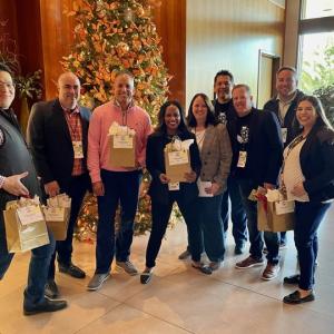 Blanca and a group of other staff each holding a bag in front of a christmas tree