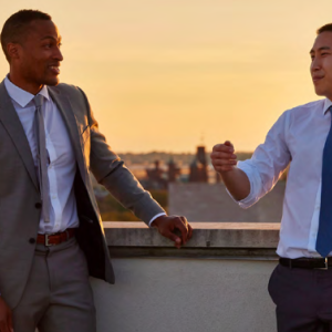 Two people in suits standing on a rooftop talking