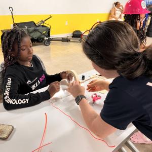 Adult volunteers and children working on building model structures with craft supplies.