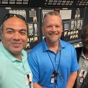 Three people posed for a selfie in front of a wall of controls.