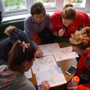 group of five people around a small table looking over maps, and other papers