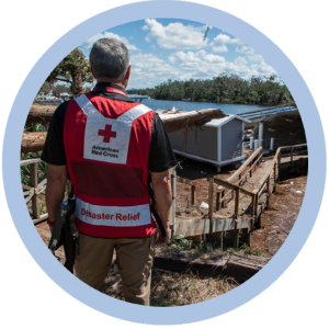 A person in a Red Cross Disaster Relief vest, looking out at damage