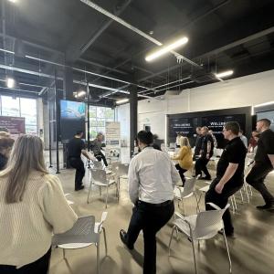 A group in a circle standing next to their chairs doing stretches.