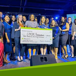 A group posed with a large check on a stage
