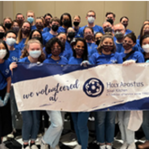 A group in matching blue shirts, masks, gloves. The front row holding a sign "We volunteered at Holy Apostus."