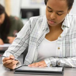 A student looking at a tablet, stylus in one hand.