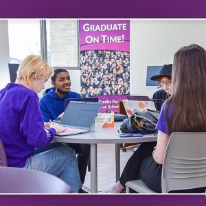 Students with open laptops seated at a circular table.