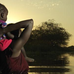 A mother in South Sudan wades through flood waters with her small child. Many refugees flee Sudan and seek shelter in South Sudan, which is burdened with its own climate shocks. / Photo by Peter Caton