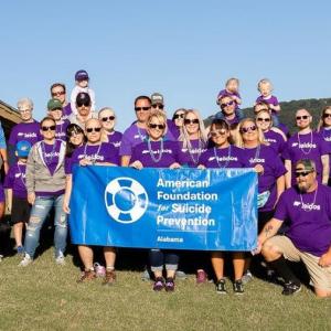 A group of people in matching shirts outdoors. Some holding a sign "American Foundation for Suicide Prevention."