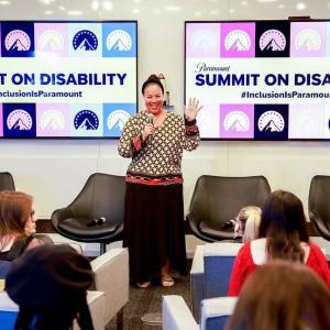 A person with a microphone waving to a group of seated people. "Summit on Disability" signs behind them.